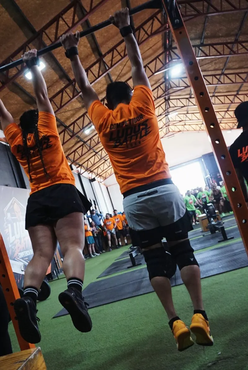 Dos personas de espaldas, con polera LUDUS, haciendo dominadas en el box de LUDUS Estación